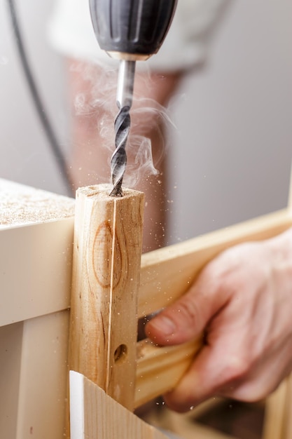 Man boort een gat elektrische boor in een houten plank thuis in de woonkamer