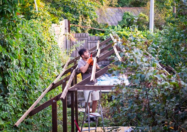 Man bouwt houten dak buitenshuis staande op ladder