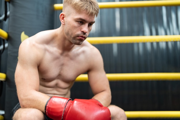 Man boxer sitting in corner on boxing ring at gym Male MMA fighter looking competitor between rounds