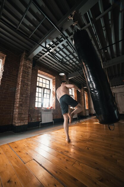 A man boxer training with a punching bag in the gym man about to kick the bag with a leg