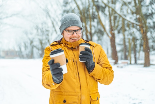 Man brengt koffie om te gaan voor vrienden in het besneeuwde stadspark. winter seizoen
