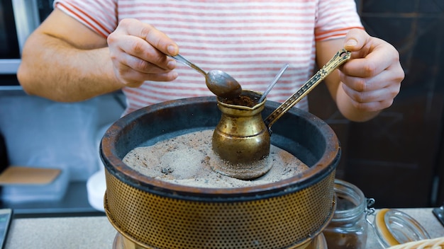 A man brews a turkish coffee traditional way on the sand in the pot called ibrik or cezve