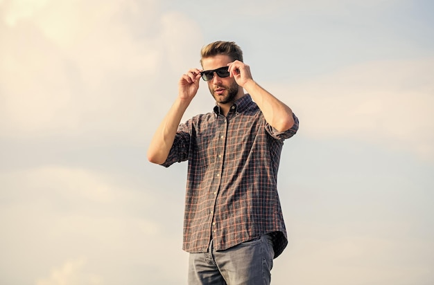 Man bril model buiten blauwe lucht achtergrond Perfecte visie Fashionista Handige man draagt zonnebril Hipster man in trendy zonnebrillend Modieuze zonnebrille Ultraviolet beschermingsconcept
