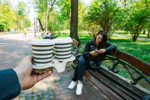 Man bring coffee for young woman date in city park