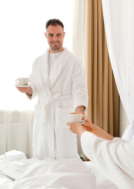 Мужчина приносит кофе своей девушке, лежащей в постели