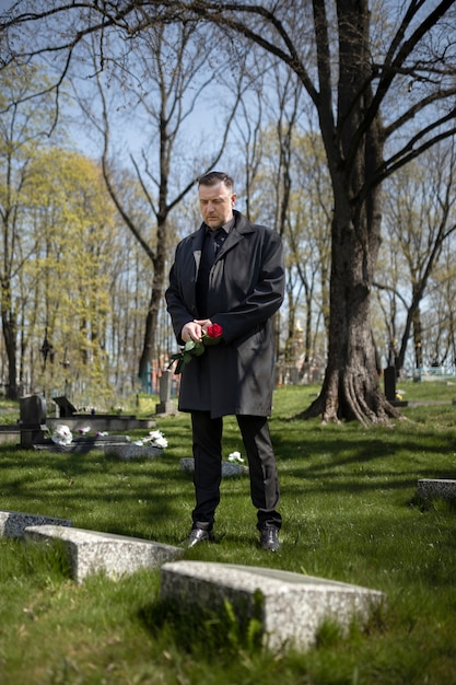 Man bringing a rose to a tombstone at the cemetery