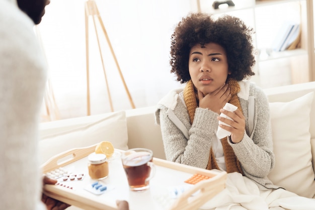 Man brings tea and medicine to sick woman sitting on couch