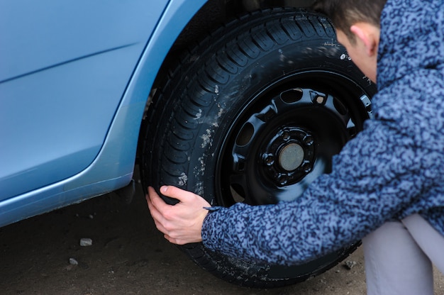 A man broke a wheel on a car and changes it on his own on the road.