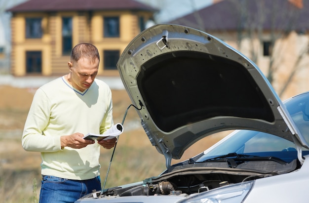 Man at  broken car reads user guide