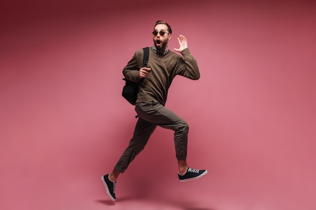 Photo man in brown outfit running on isolated background and holding backpack