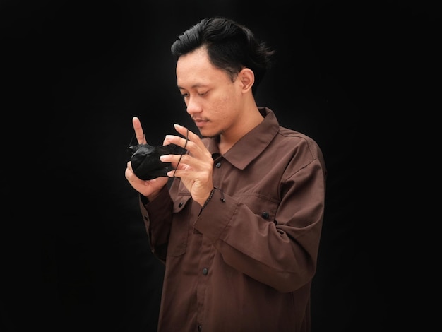 A man in a brown shirt holds a small black object in his hand.