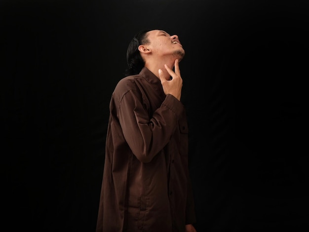 A man in a brown shirt stands in front of a black background.