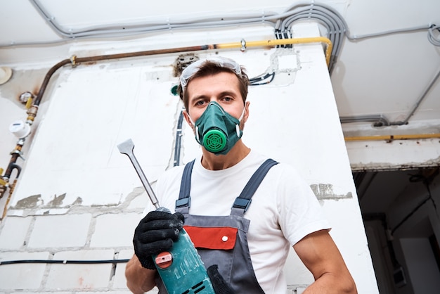 Man in builder uniform with hammer drill make repairs in the
room.