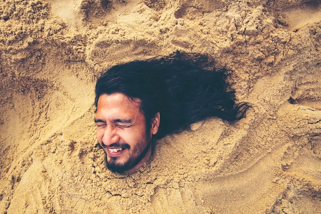 Uomo sepolto nella sabbia in spiaggia. concetto di felicità, vacanza, tutto va bene.