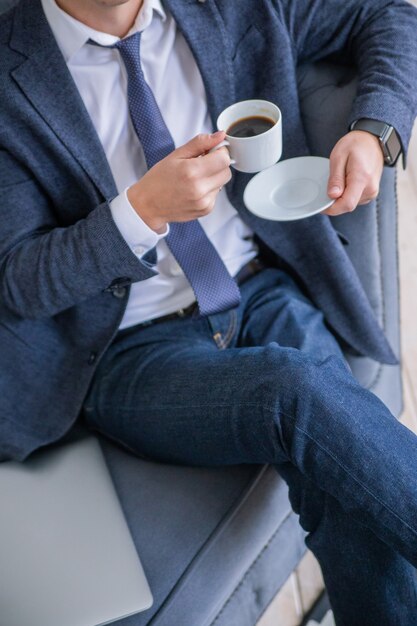 A man in a business suit holds a cup of coffee in his hands