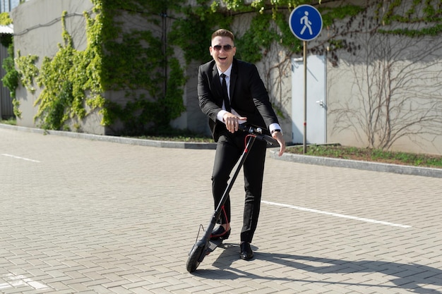 Man in a business suit is having fun and laughing near an electric scooter