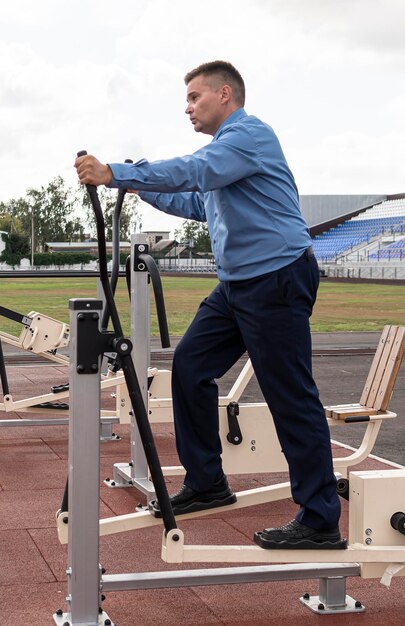 Man in a business suit is warming up on simulators at the stadium Sports exercises after office work The fight against excess weight Businessman in the gym