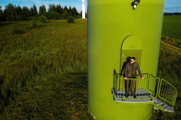 A man in a business suit with a green Golf shirt stands next to a windmill against the background of the field and the blue sky.Businessman near the windmills.Modern concept of the future.