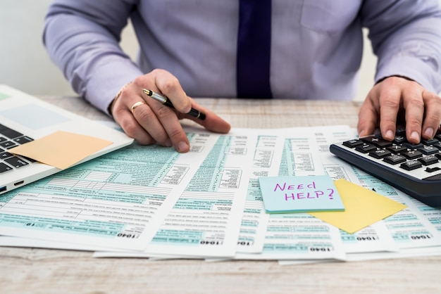 A man in a business suit writes a 1040 tax form in the office. Male hands fill on paper with calculator at workplace. Accounting concept