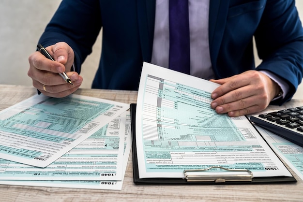 A man in a business suit writes a 1040 tax form in the office. Male hands fill on paper with calculator at workplace. Accounting concept