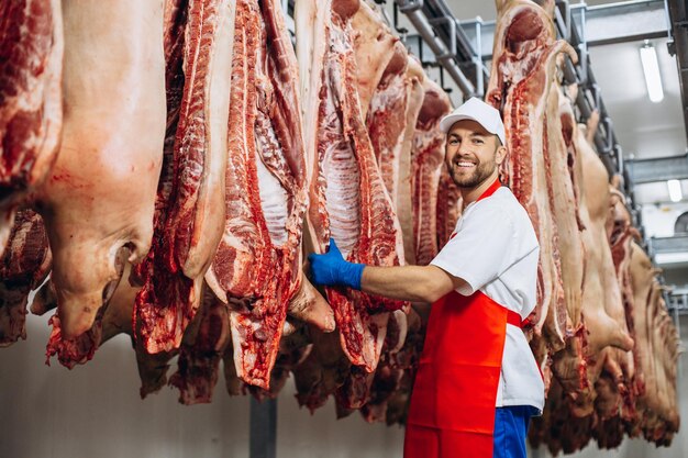 Man butcher standing by the hanging meat at the freezer