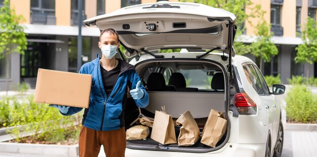 Man by the car. Guy in a delivery uniform. Man in a medical mask. Coronavirus concept.