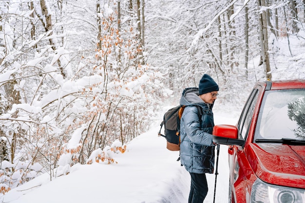 man by red car in winter forest