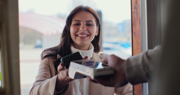 Man café-eigenaar ondernemer koffie zetten voor een klant in een café Vrouwelijke klant betaalt voor afhaalkoffie met contactloze NFC-betalingstechnologie op smartphone Klant gebruikt mobiel om te betalen