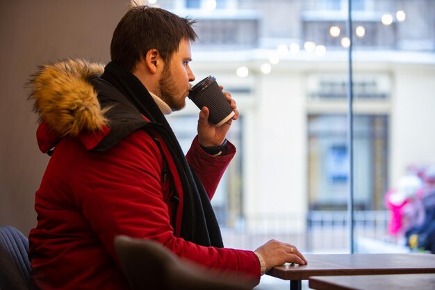 Foto uomo in caffè con cappotto rosso d'inverno che beve tè che si riscalda dentro