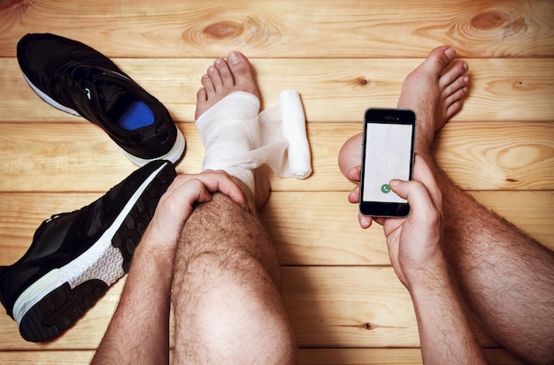 The man calls the emergency services sitting on the wooden\
floor. sports injuries. top view