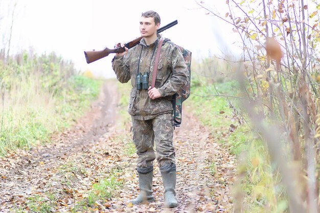 春の狩りで森のベルトにカモフラージュと銃を持った男