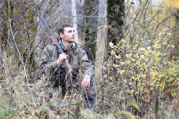 春の狩りで森のベルトにカモフラージュと銃を持った男