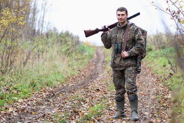 春の狩りで森のベルトにカモフラージュと銃を持った男