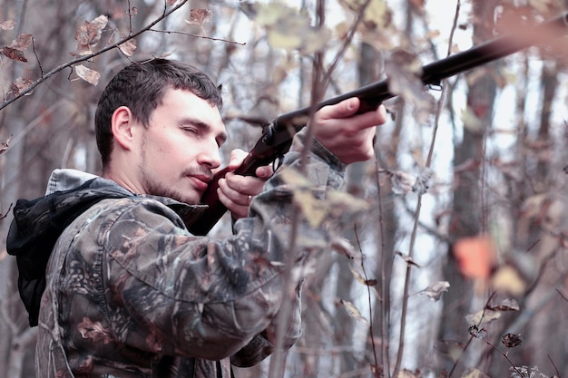 Photo man in camouflage and with a hunting rifle in a forest on a spring hunt