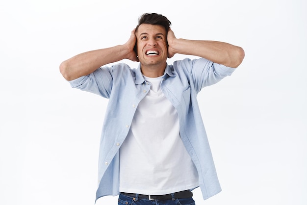 Man cant stand his noisy loud neighbours upstairs Portrait of annoyed angry man arguing yelling at person on top raising head clench teeth irritated and shut ears white background