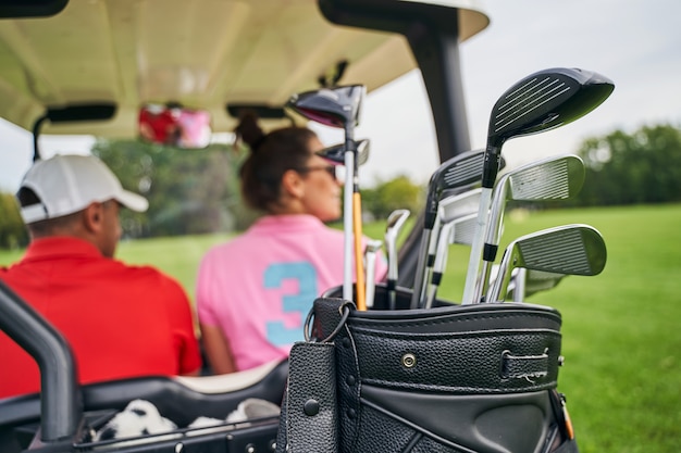 Man in a cap and a dark-haired woman riding in a golf car