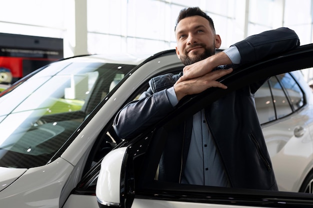 A man in a car dealership dreamily hugs the door of a new car