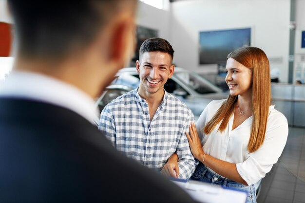 Photo man car salesman telling about the features of the new car to the couple