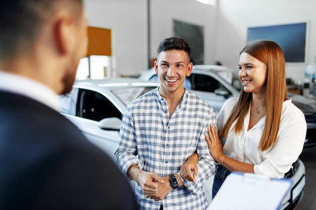 Man car salesman telling about the features of the new car to the couple