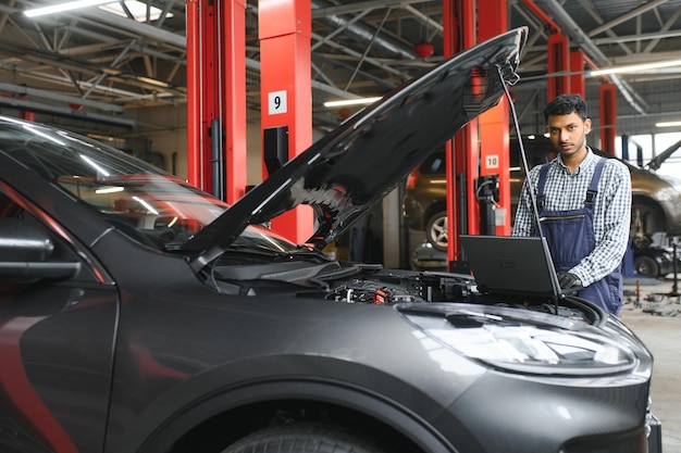 車のガレージでのメンテナンスと修正のためにタブレット コンピューターを使用して詳細をチェックするシステム中にエンジンの車の問題を修復する男性自動車技術者メカニック