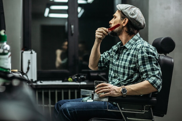 man  carefully brushing his beard while being in a modern barbershop