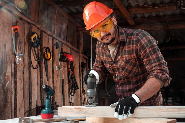 A man carpenter cuts a wooden beam using an electric jigsaw, male hands with an electric jigsaw closeup.