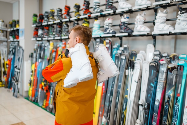 Man carries on his shoulder ski or snowboarding boots in sports shop