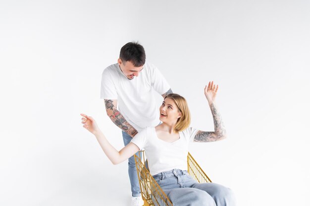 Man carries a woman in a shopping cart on a white background Cheerful young couple