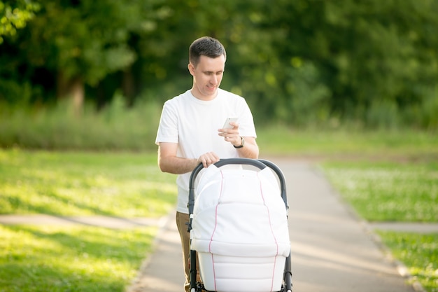 Photo man carrying a baby stroller while looking a smartphone