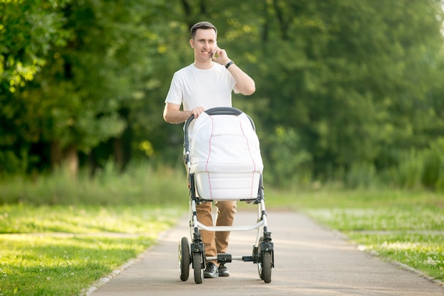 Photo man carrying a baby stroller white talking on phone