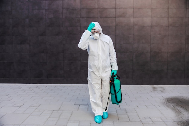 Man carrying sprayer with disinfectant and holding his head. Protection from coronavirus concept.