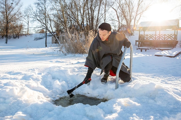 Man carving out a hole in the ice with an axe for winter swimming in cold sunny winter day