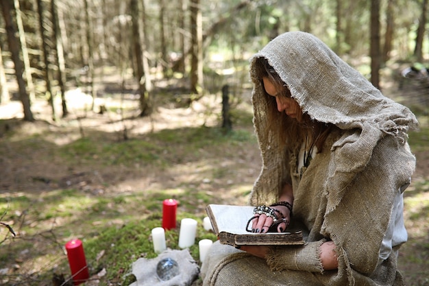 Un uomo in tonaca trascorre un rituale in una foresta oscura con una sfera di cristallo e un libro