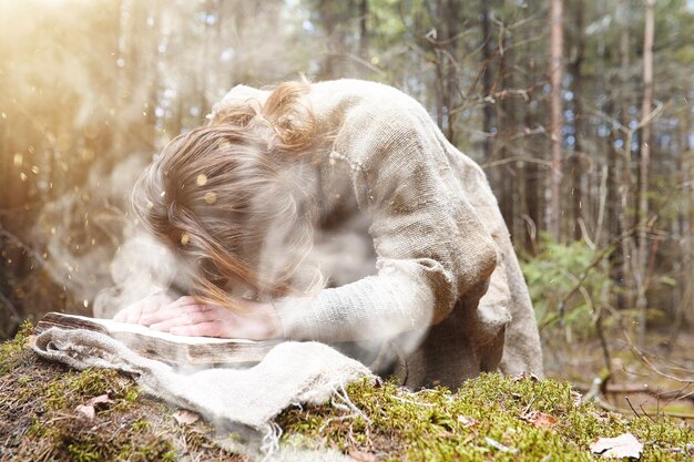 A man in a cassock spends a ritual in a dark forest with a crystal ball and book